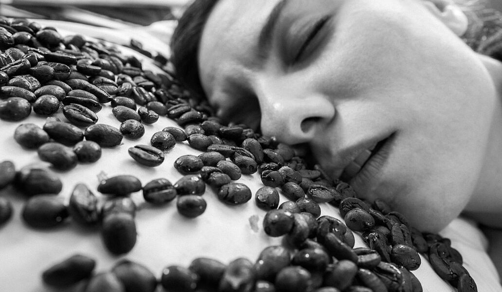 Schlafende Frau auf Kaffeebohnen Eine Frau schläft auf einem Berg aus Kaffeebohnen – ein Bild für müde Routinen und das Risiko, im Arbeitsalltag das Wesentliche zu verschlafen: Beziehung, Menschlichkeit und echte Verbindung.Schlafende Frau auf Kaffeebohnen – Sinnbild dafür, was wir im Businessalltag nicht verschlafen dürfen: das Miteinander.